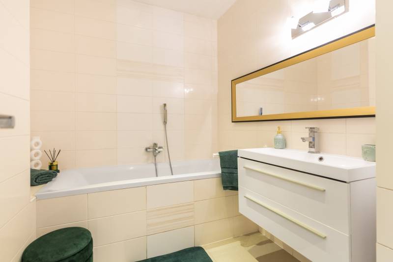 Fürdőszoba tükörrel, káddal és mosdóval egy családi házban, világos csempékkel.