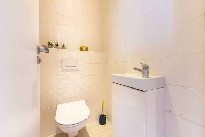 Fürdőszoba mosdóval és WC-vel egy családi házban, világos csempék, dekorációk.