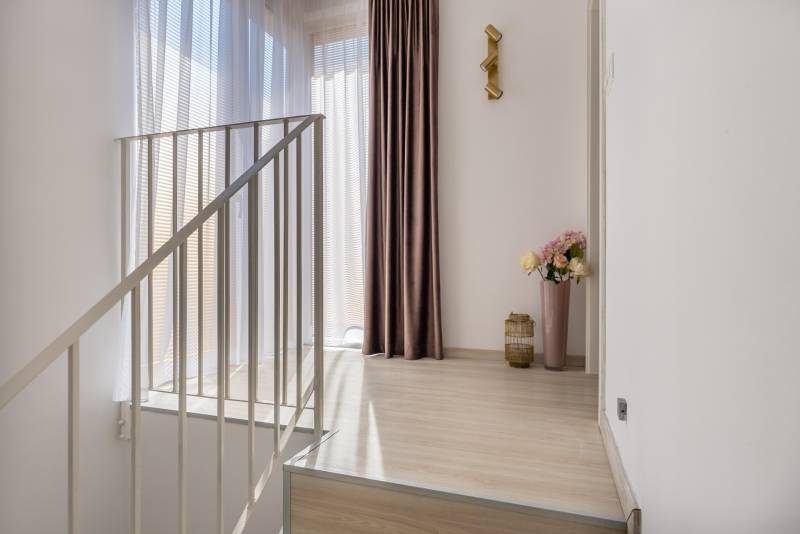 Családi ház belső tere fa dekor padlóval, függönyökkel és dekoratív világítással.