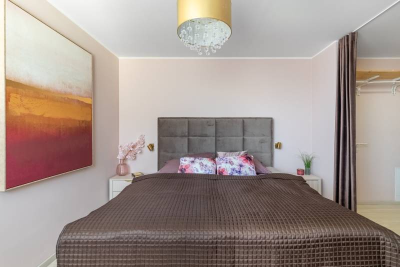 Hálószoba széles ággyal, dekoratív párnákkal, képpel és rejtett tárolóhellyel egy 4 szobás lakásban.