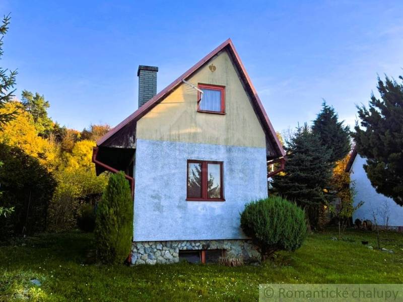 Házikó Sološnicában, zölddel körülvéve, kék vakolattal és ferde tetővel.