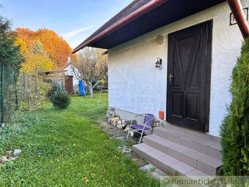 Ház Sološnicában gyepes udvarral és fákkal a színes őszi tájban.