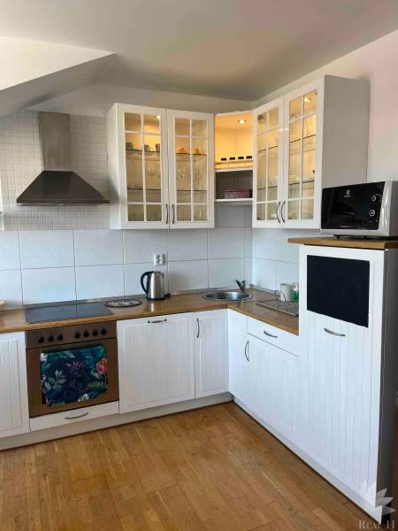 Konyha egy háromszobás lakásban fa padlóval, fehér szekrényekkel és tárolóhellyel.