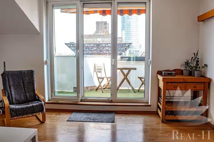 Nappali erkéllyel, fa padló, szék és asztal egy háromszobás lakásban.