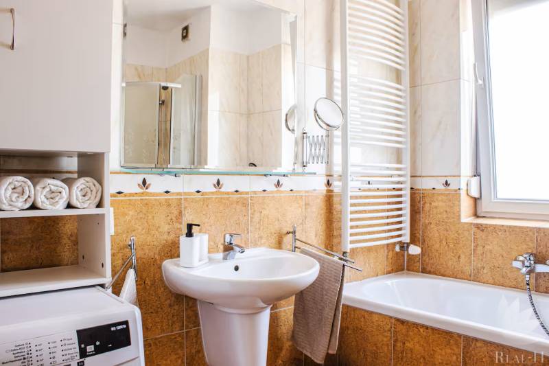 Fürdőszoba egy háromszobás lakásban mosdóval, káddal, mosógéppel és törölközőszárítóval.