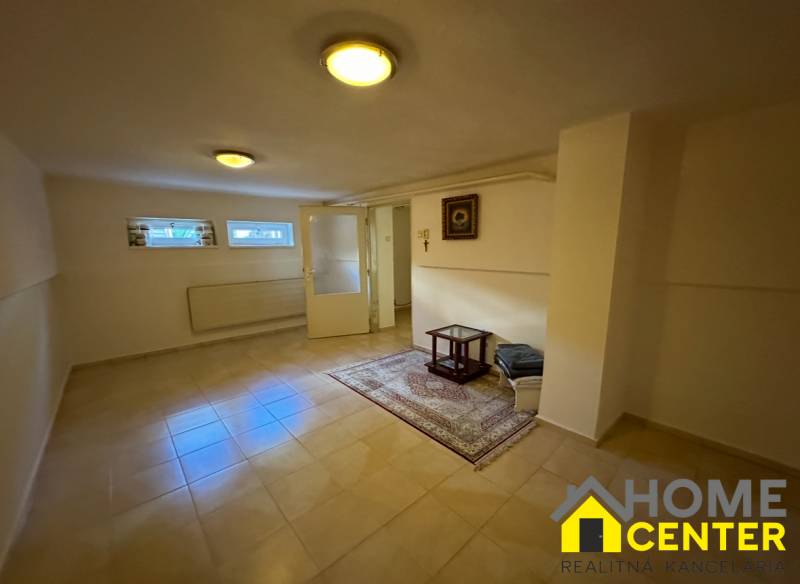 Családi ház belső tere járólappal, szőnyeggel, kis ablakokkal és egyszerű asztallal.