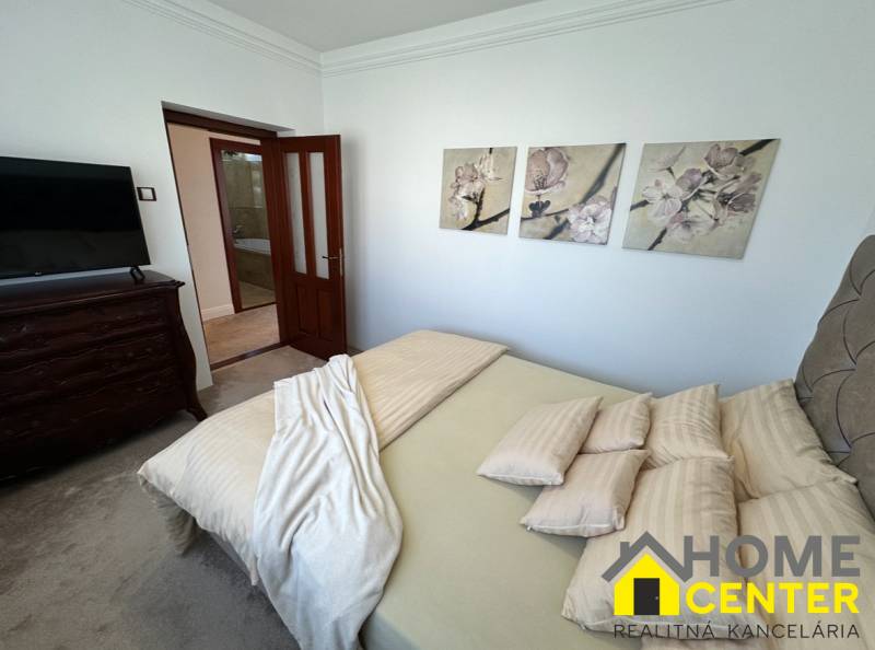 Családi ház hálószobája dekoratív képekkel a falon, kárpitozott bútorokkal és ajtókkal.