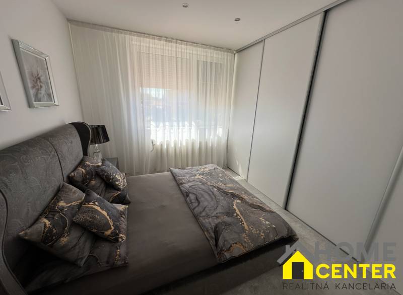 Hálószoba családi házban sötét ágyneművel és nagy szekrénnyel.