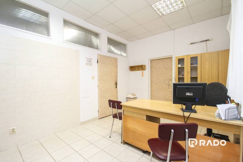 Irodák íróasztallal, székkel, számítógéppel és szekrénnyel világos kerámia padlón.