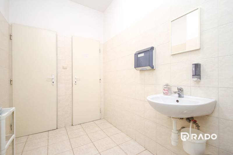 Iroda mosdóval, adagolókkal és tükörrel. Fehér csempék, világos padló.