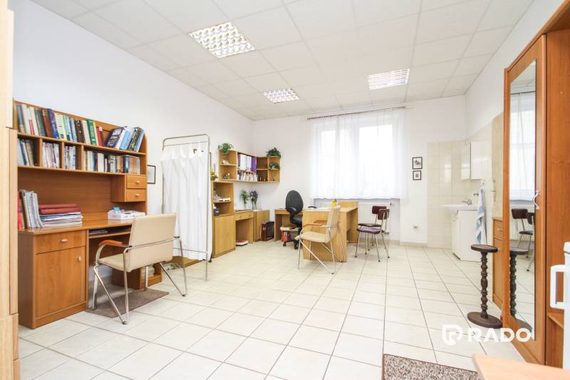 Irodák asztalokkal és székekkel, fehér kerámia padló, polcok könyvekkel.