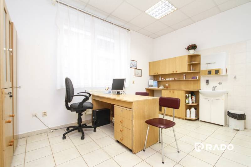 Iroda számítógéppel, asztallal és székkel, világos belső tér, polcok és mosdó.