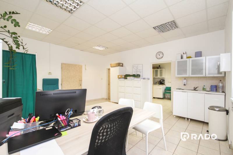 Iroda bútorokkal, számítógéppel és konyhával, a padlón csempék vannak.