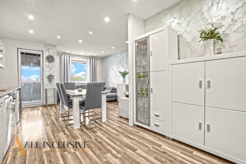 Világos belső tér háromszobás lakásban, fa dekorációjú padlóval és fehér bútorokkal.