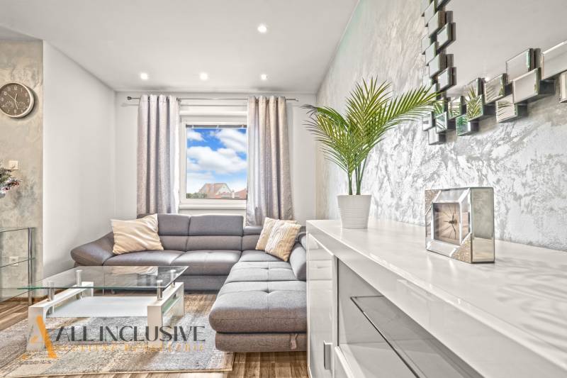 Nappali szürke kanapéval, üvegasztallal és fa dekorációjú padlóval.