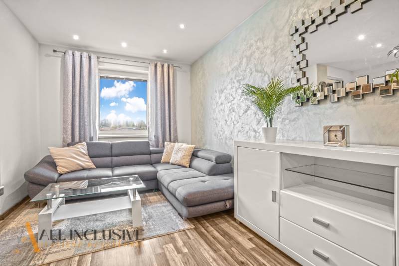 Nappali egy háromszobás lakásban kényelmes kanapéval és fa dekorációjú padlóval.