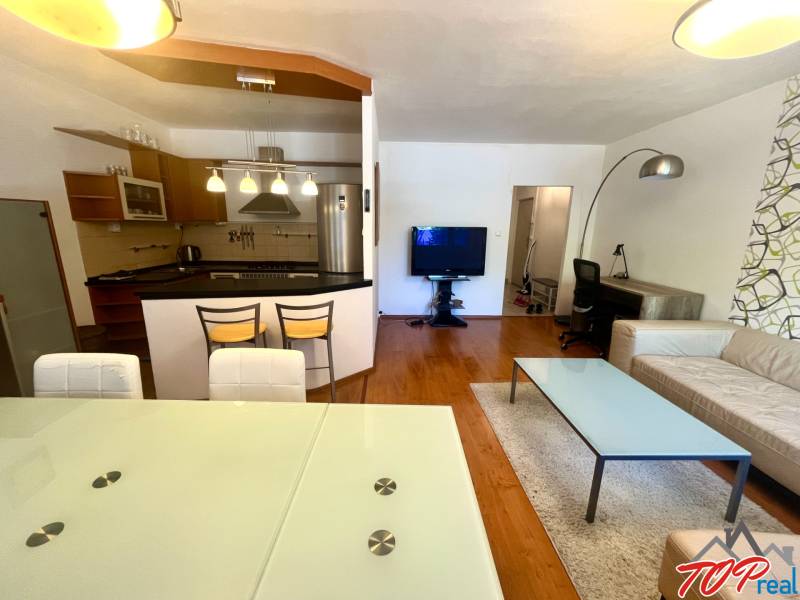 Nappali egy háromszobás lakásban konyhával, étkezőasztallal és kényelmes ülőgarnitúrával.