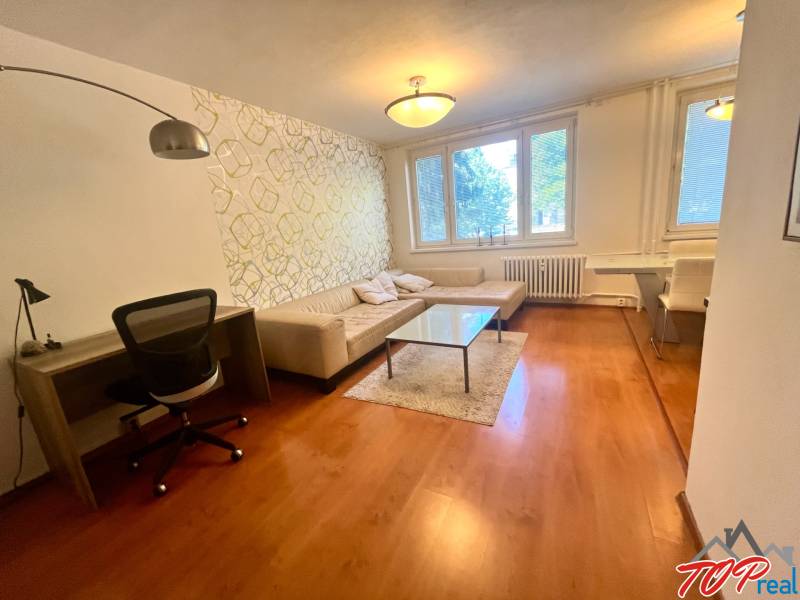 Nappali egy háromszobás lakásban kanapéval, asztallal és íróasztallal.