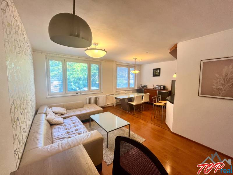 Nappali egy háromszobás lakásban kanapéval, asztallal és étkező sarokkal.