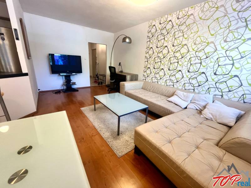 Nappali bézs kanapéval és televízióval egy háromszobás lakásban.