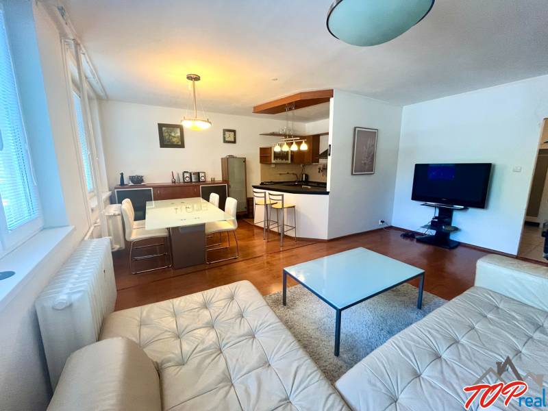 Nappali konyhával egy háromszobás lakásban, felszerelés tartalmazza a kanapét, az asztalt és a televíziót.