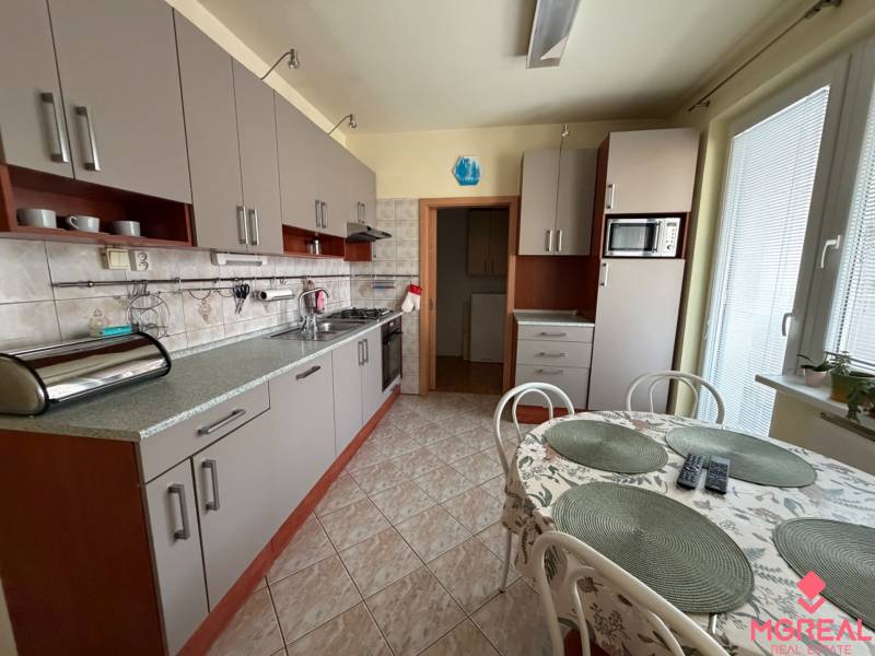 Konyha világosszürke szekrényekkel egy háromszobás lakásban, étkezőasztallal kiegészítve.