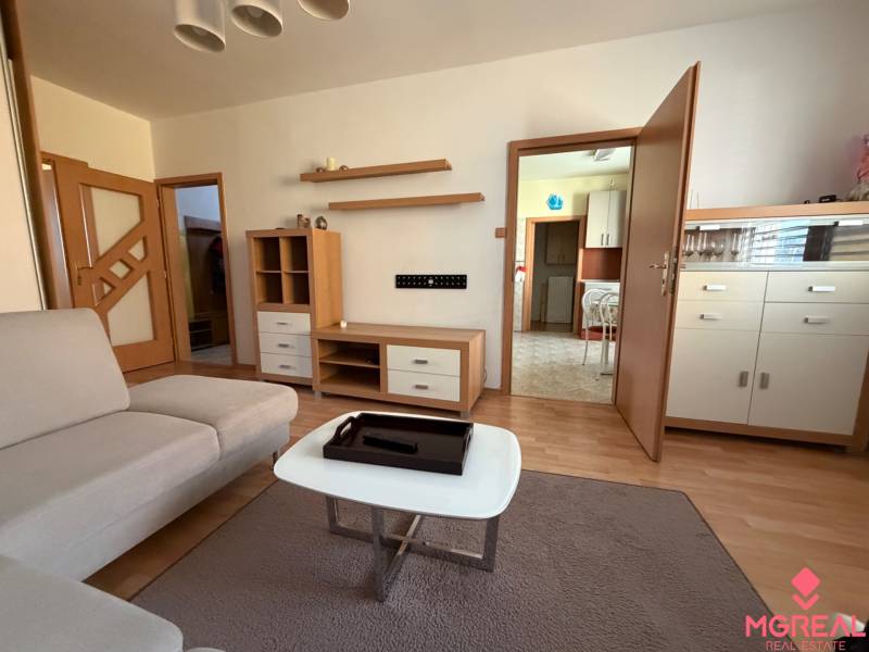 Nappali egy háromszobás lakásban kanapéval és fa dekor padlóval.