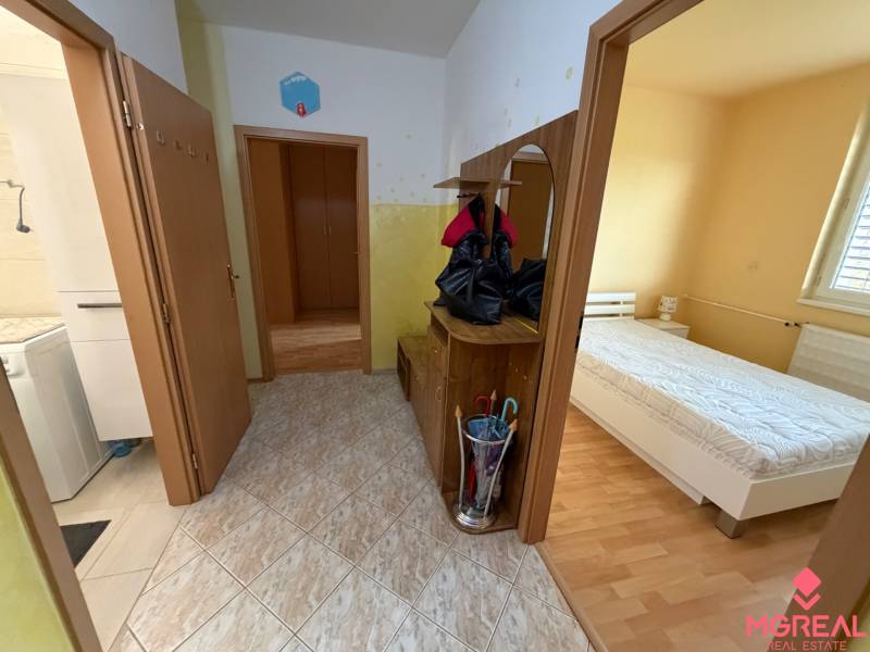 Folyosó egy háromszobás lakásban, járólappal, fürdőszobába és hálószobába nyíló bejárattal, fa dekor padlóval.