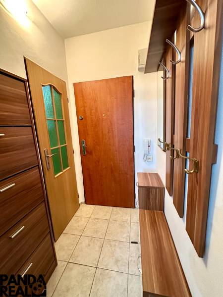 Garzonlakás előszobával, fa ajtókeretekkel és csempével, elegáns dizájn és praktikus tárolóhelyek.