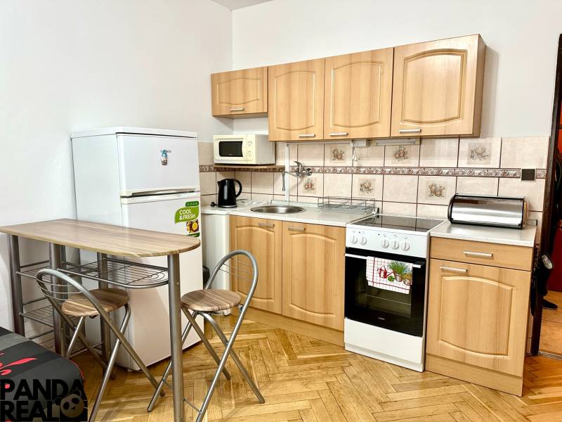 Konyha garzonlakásban fa mintázatú padlóval, háztartási gépekkel és ülőhellyel.