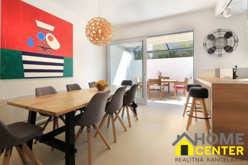 Világos étkező a villában, faasztallal, színes festménnyel és terasszal.