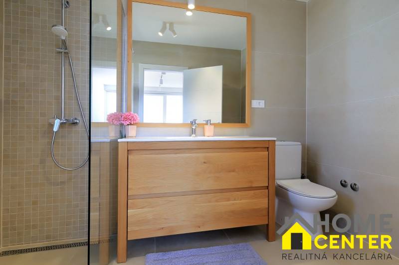 Fürdőszoba a villában fa dekorációval, zuhanyzóval és nagy tükörrel ellátott mosdóval.