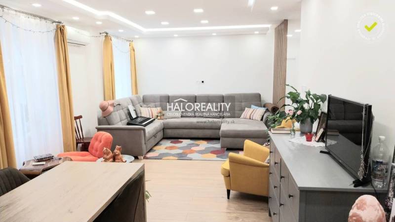 Nappali egy háromszobás lakásban fa dekor padlóval, szürke kanapéval és sárga fotellel.