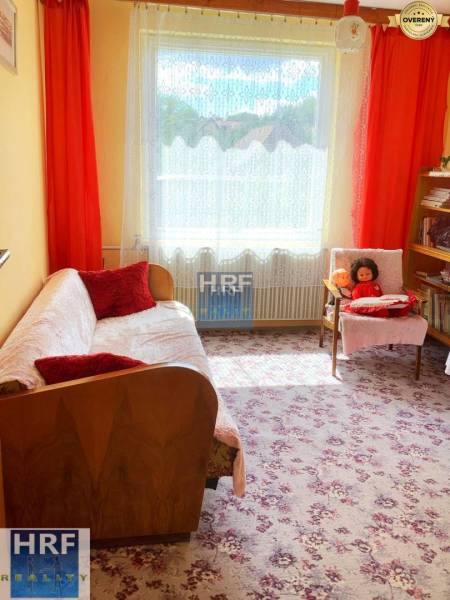 Szoba egy családi házban virágos szőnyeggel, kanapéval és polcokkal.