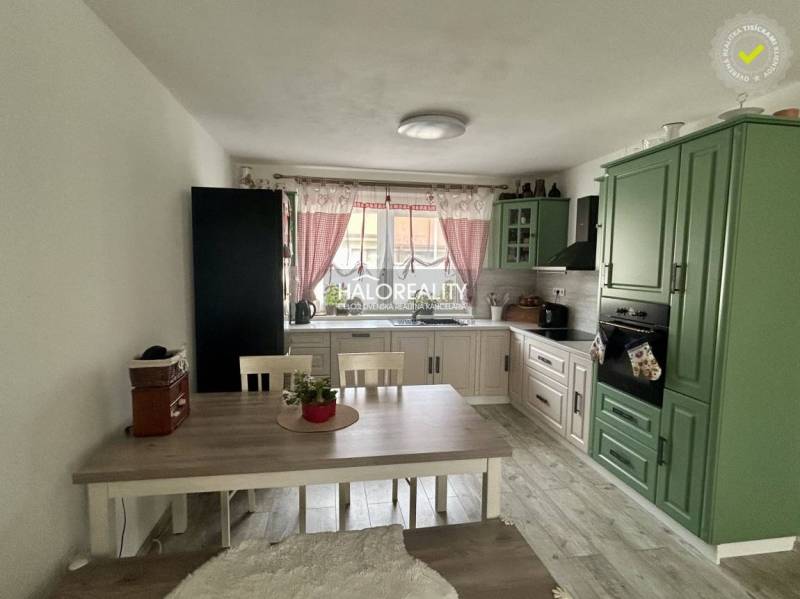 Konyha családi házban zöld konyhabútorral, étkezőasztallal és piros függönyökkel.