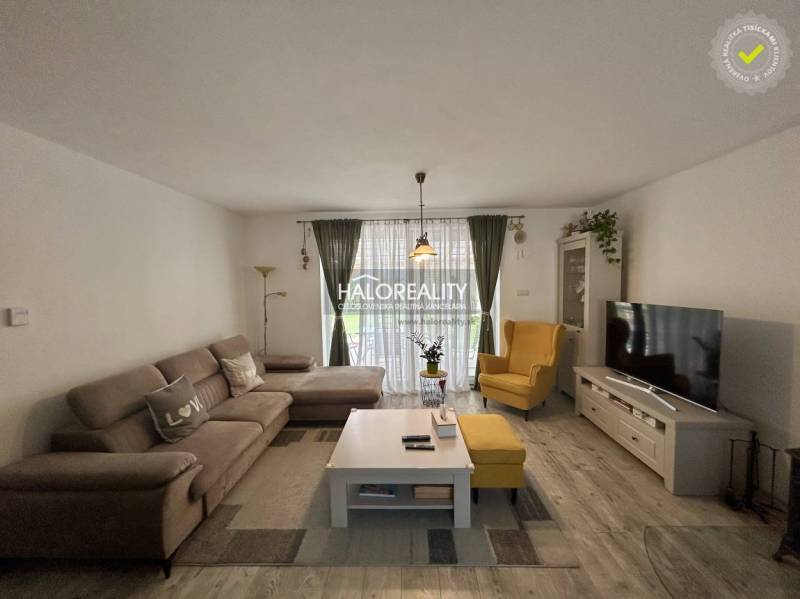 Nappali egy családi házban kanapéval, fotellel, televízióval és virágokkal.