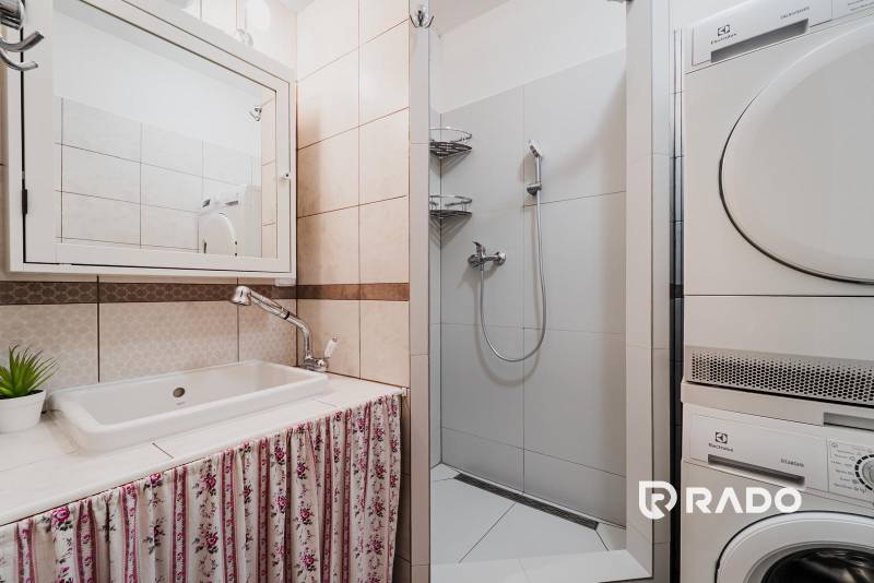 Fürdőszoba egy háromszobás lakásban mosógéppel, zuhanyzóval és függönyös mosdóval.