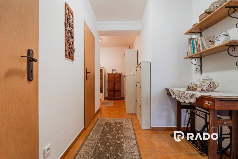 Előszoba egy háromszobás lakásban csempével, fa polccal és dekoratív tárgyakkal.