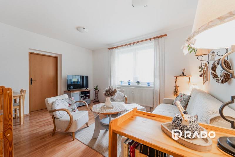 Nappali egy háromszobás lakásban kényelmes bútorokkal és fa mintázatú padlóval.