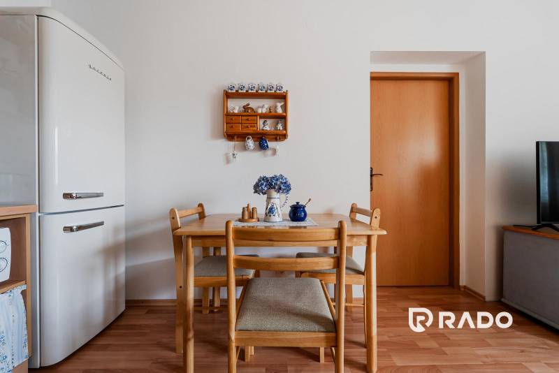 Étkezőasztal székekkel, hűtőszekrény és fa mintázatú padló a háromszobás lakásban.