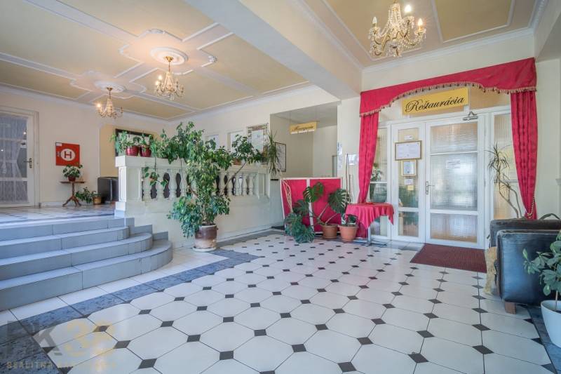 Szállodai recepció növényekkel és csillárokkal, geometriai mintás padlóburkolat.