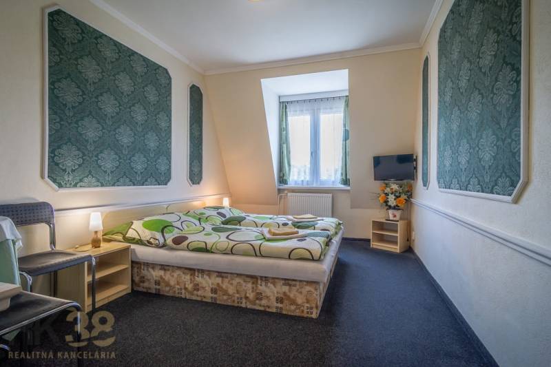 Kétszemélyes ággyal, szőnyegpadlóval, televízióval, székkel és dekorációkkal ellátott szoba szállodákban és panziókban.