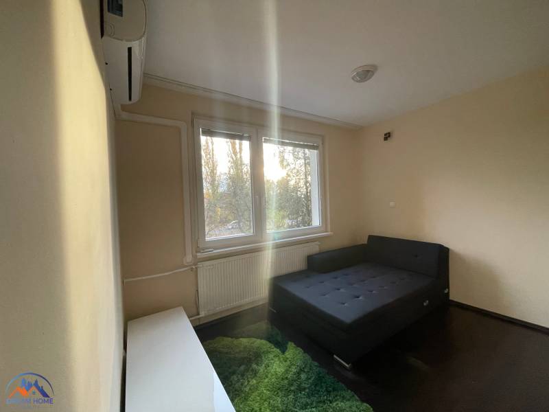 Egyszerű szoba ággyal, szőnyeggel és ablakkal egy egyszobás lakásban.