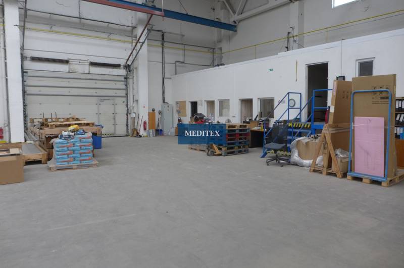 Egy raktár belseje magas mennyezettel, összecsukható kapukkal és különféle árukkal raklapokon.