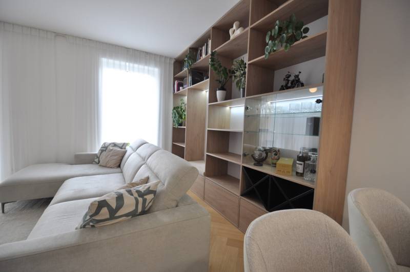 Nappali egy családi házban fehér kanapéval, fa könyvespolccal és növényekkel.