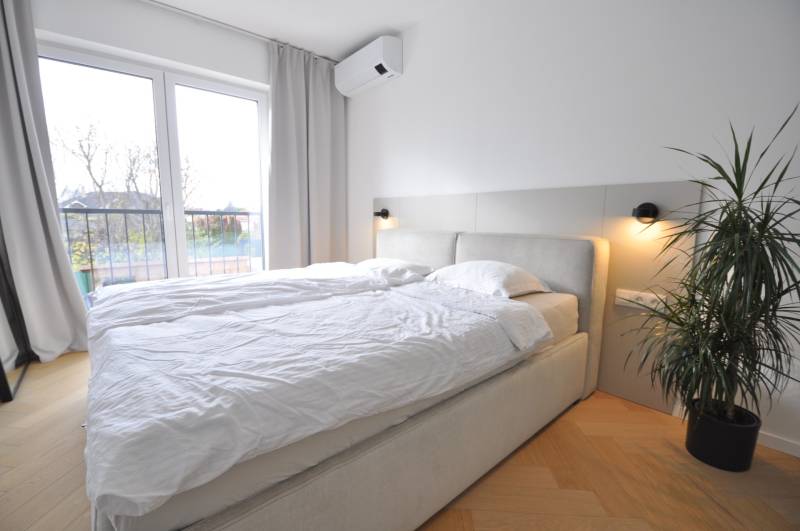 Hálószoba családi házban ággyal, növénnyel és fa dekorációjú padlóval.