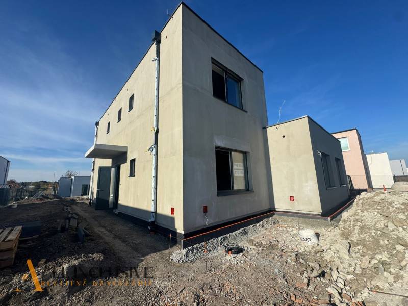 Hubicai családi ház építés alatt, minimalista külsővel és szomszédos épületekkel.