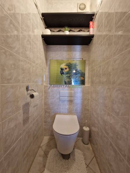 Csempefalú WC papagájképpel és polcokkal egy háromszobás lakásban.