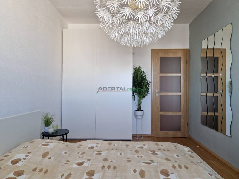 Hálószoba dekoratív lámpával, gardróbszekrénnyel és fa mintázatú padlóval egy háromszobás lakásban.