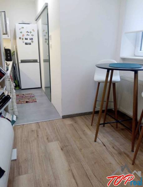 Konyha egy egyszobás lakásban fa dekorációjú padlóval, magas asztallal és székekkel.